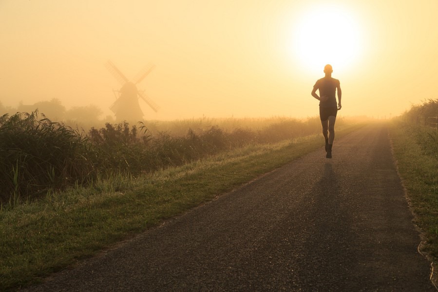 Man running in the foggy, Dutch countryside near a windmill.